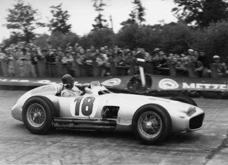 Black and white photo of Juan Manual Fangio driving the Mercedes W1969R